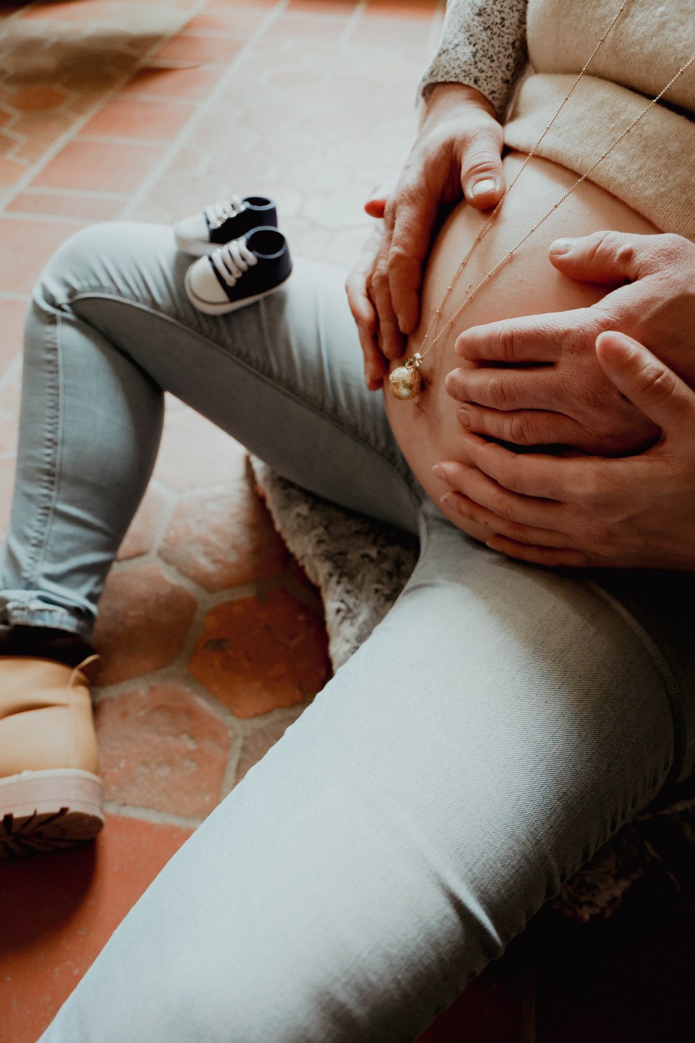 Grossesse — ventre entouré des mains, petites chaussures de bébé posées à côté