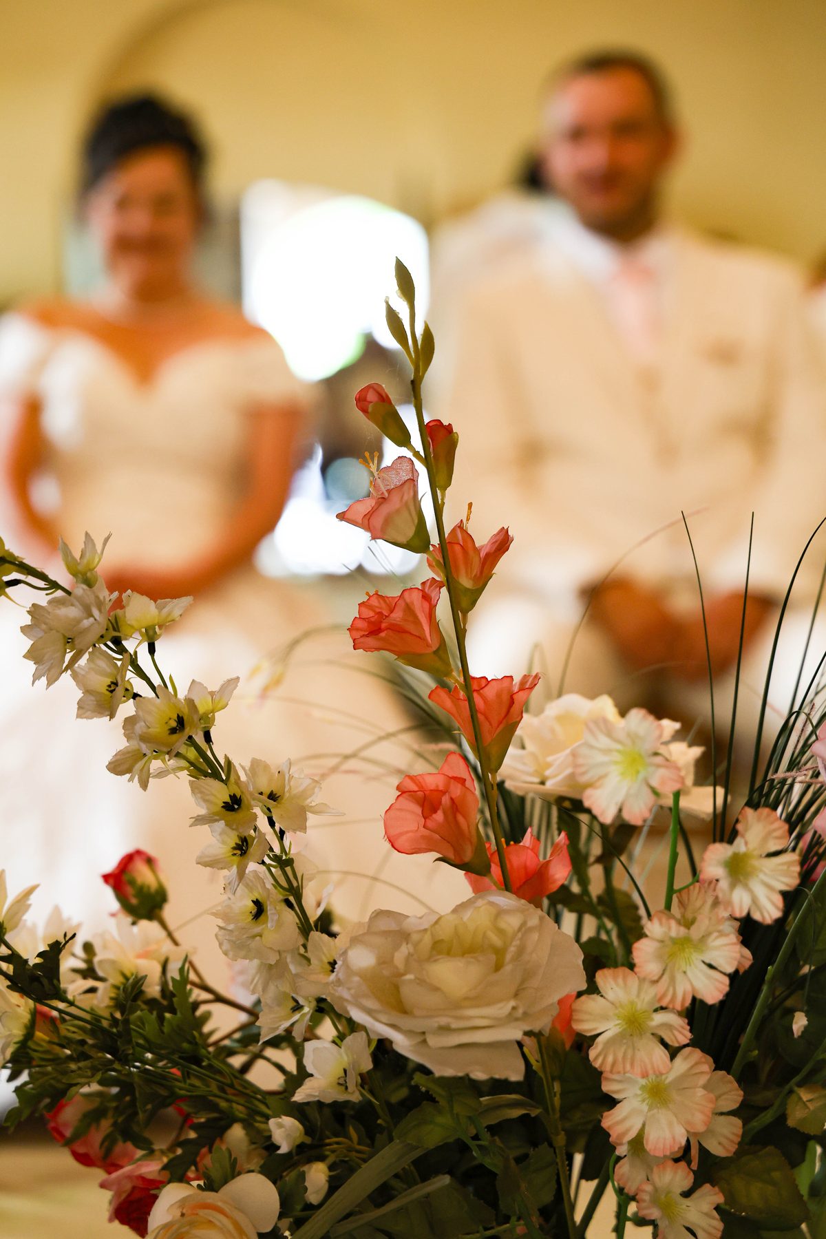 Mariage — fleurs corail au premier plan, mariés en arrière-plan