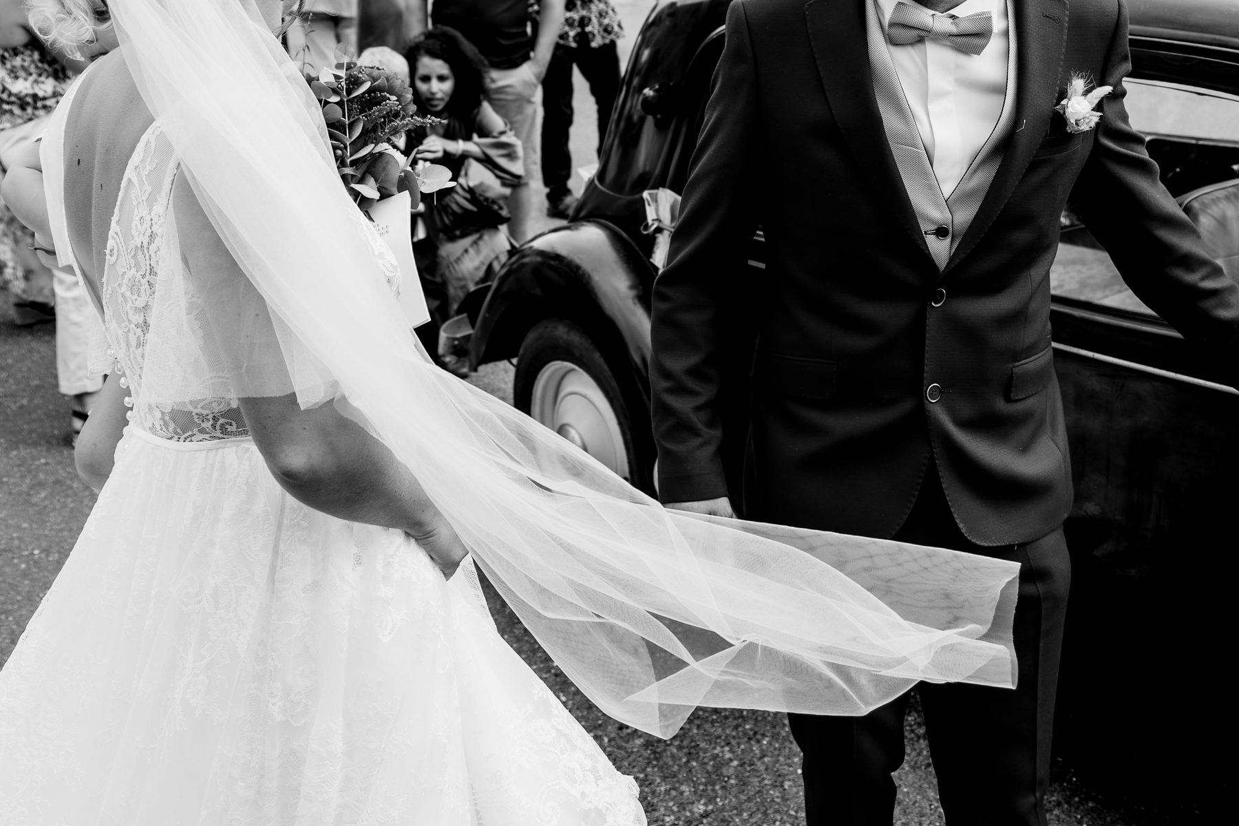 Mariage — le voile de la mariée s'envole devant la voiture ancienne, noir et blanc