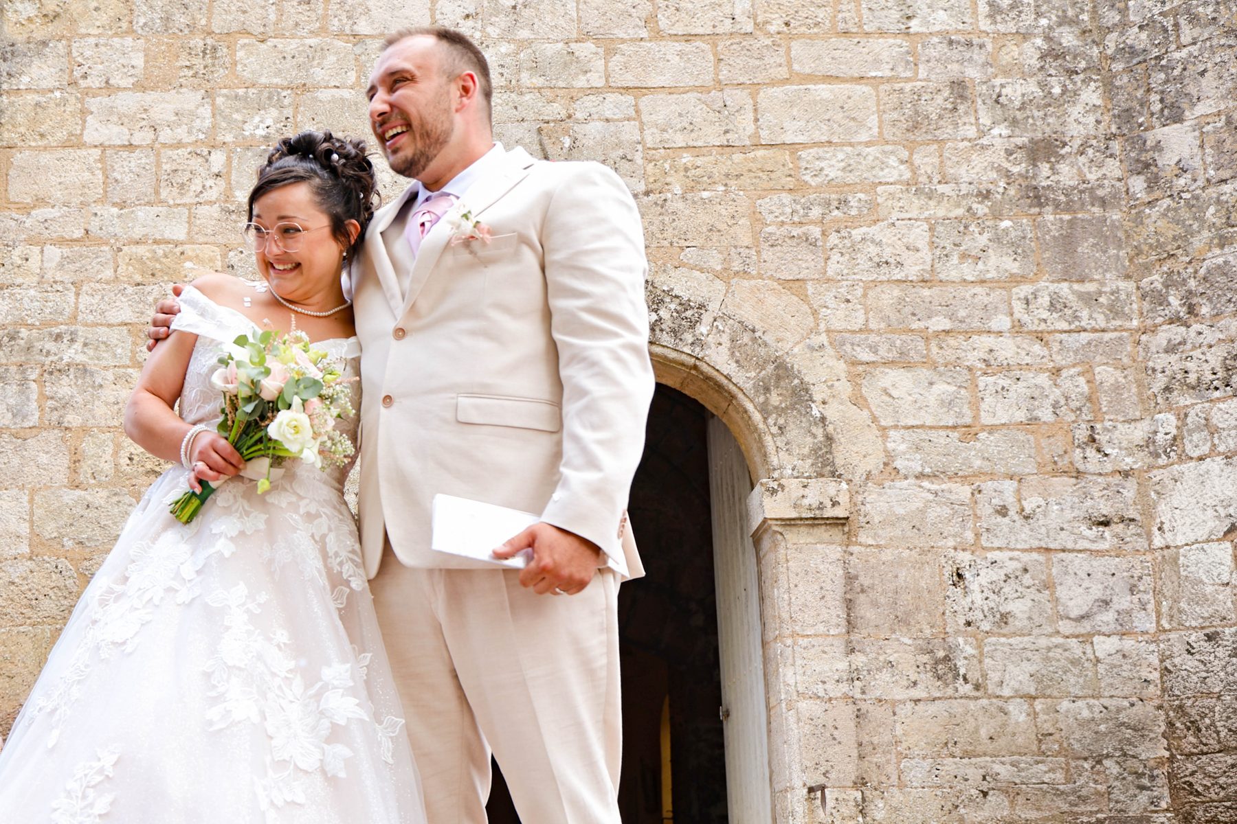Mariage — les mariés riant devant le mur en pierre de l'église