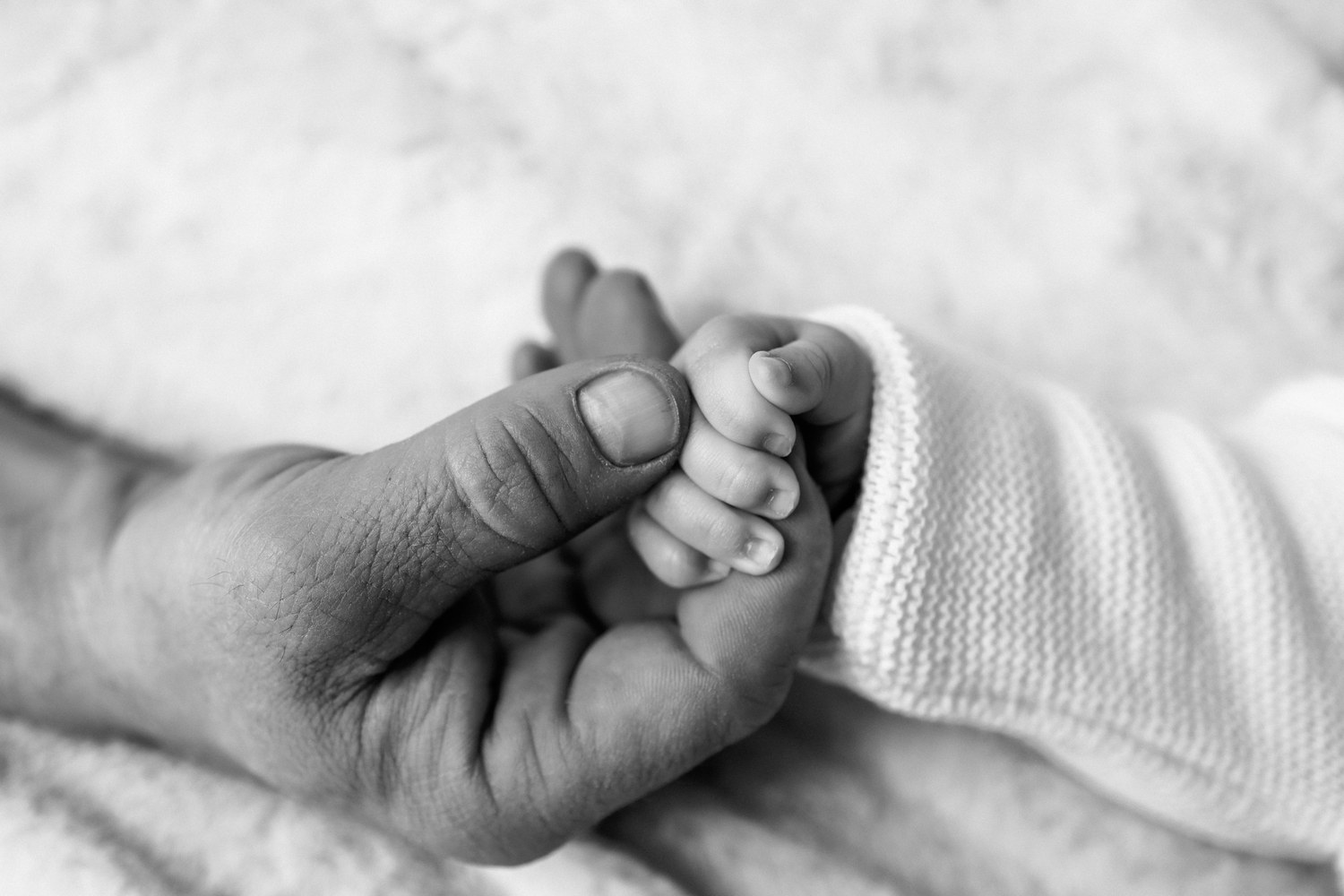 Naissance — petit pied du nouveau-né tenu dans la main d'un parent, noir et blanc