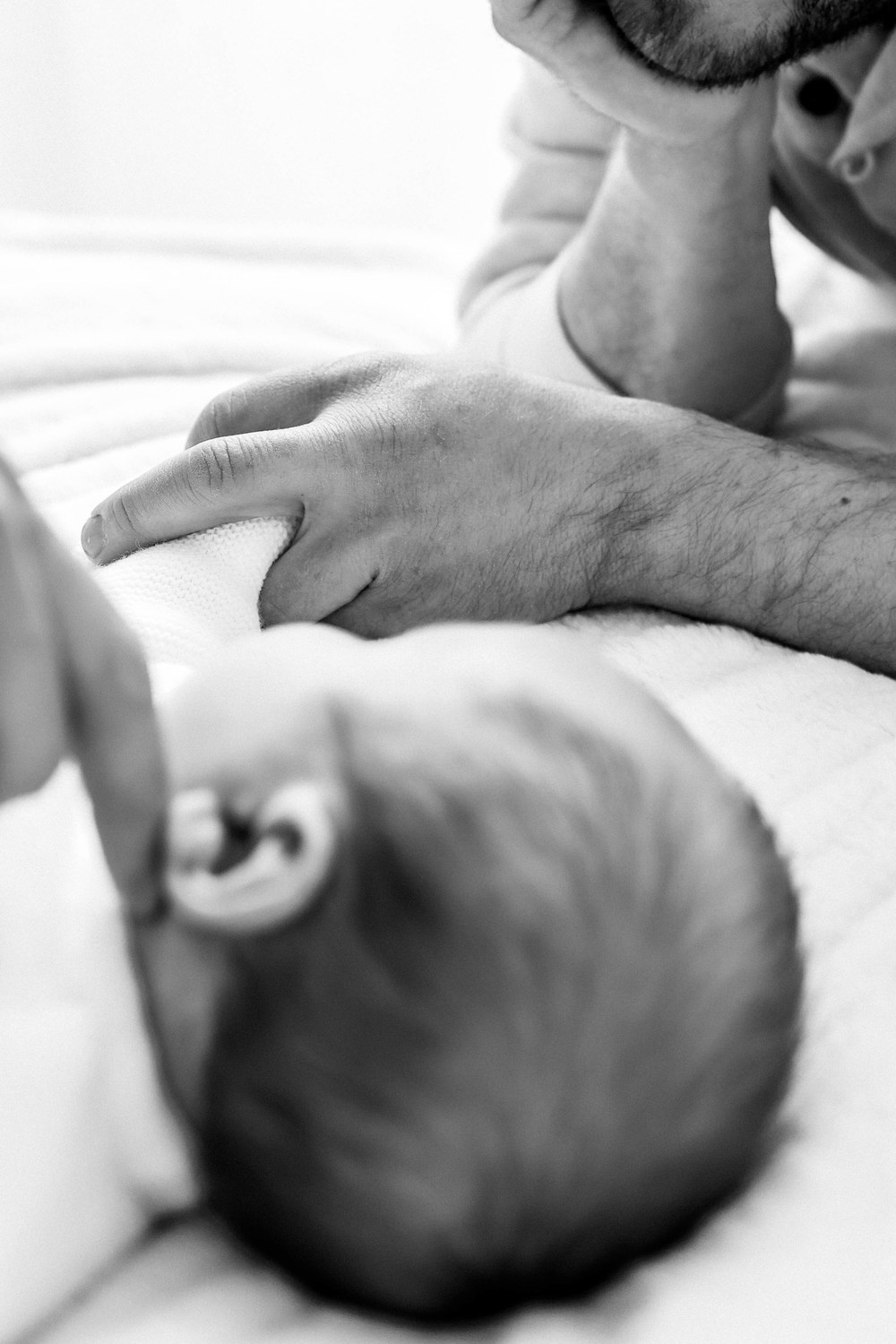 Naissance — main d'un parent posée près de la tête du nouveau-né, noir et blanc